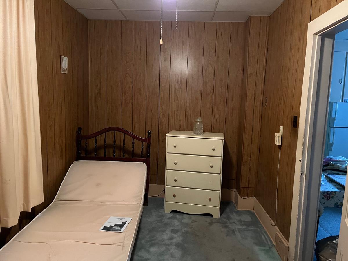 Erie PA bedroom — wood paneling throughout, original bed and dresser, single bulb lighting